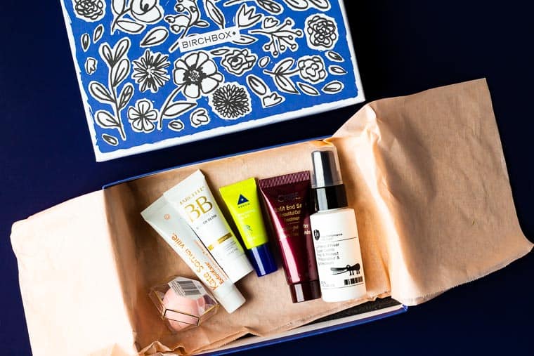 May 2020 Birchbox opened with the lid above and the samples on a piece of peach tissue paper over a blue background
