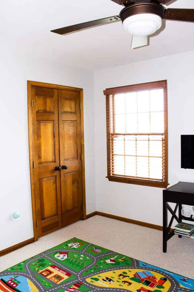Closet door, window with wood blinds, part of a road rug and a table