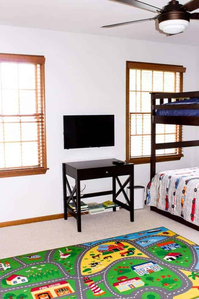 Road rug, desk and tv between 2 windows and part of a bed showing
