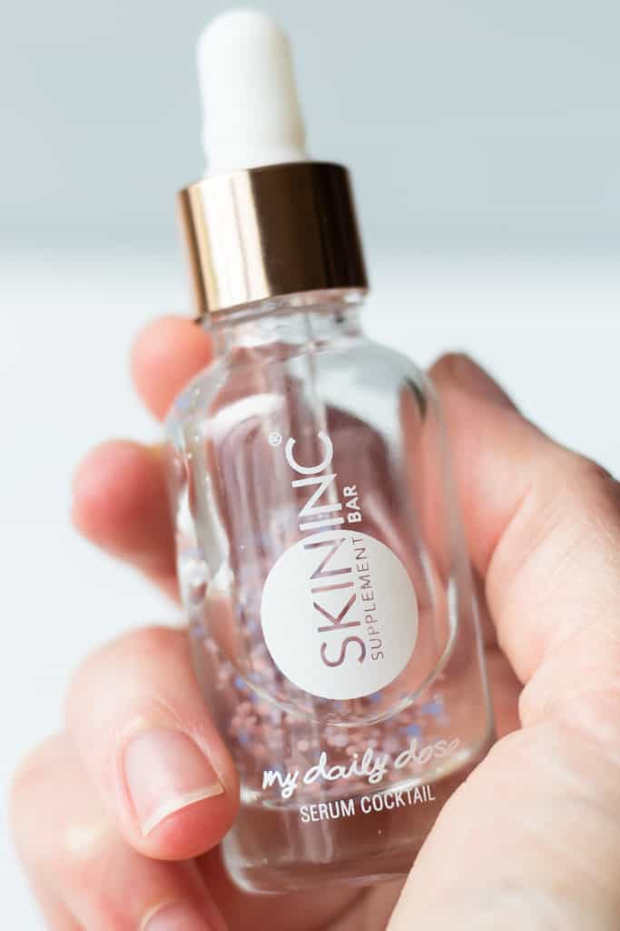 Skin Inc. My Daily Dose of Glow serum bottle being held up over a light background