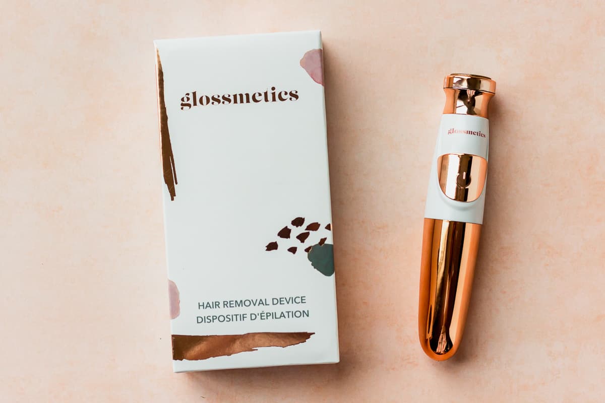 Glossmetics Hair Removal Device and it's package on a peach backdrop