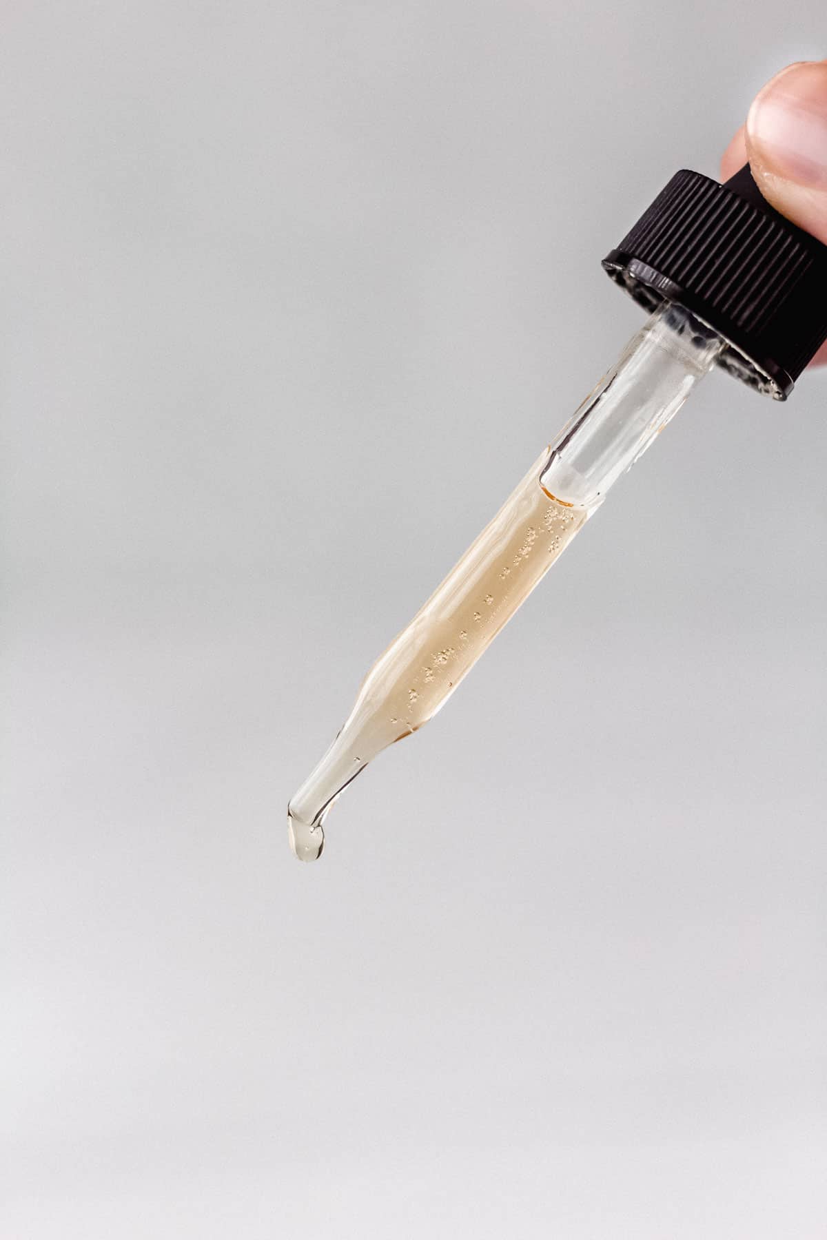A dropper with caffeine solution dripping out of it with a gray backdrop