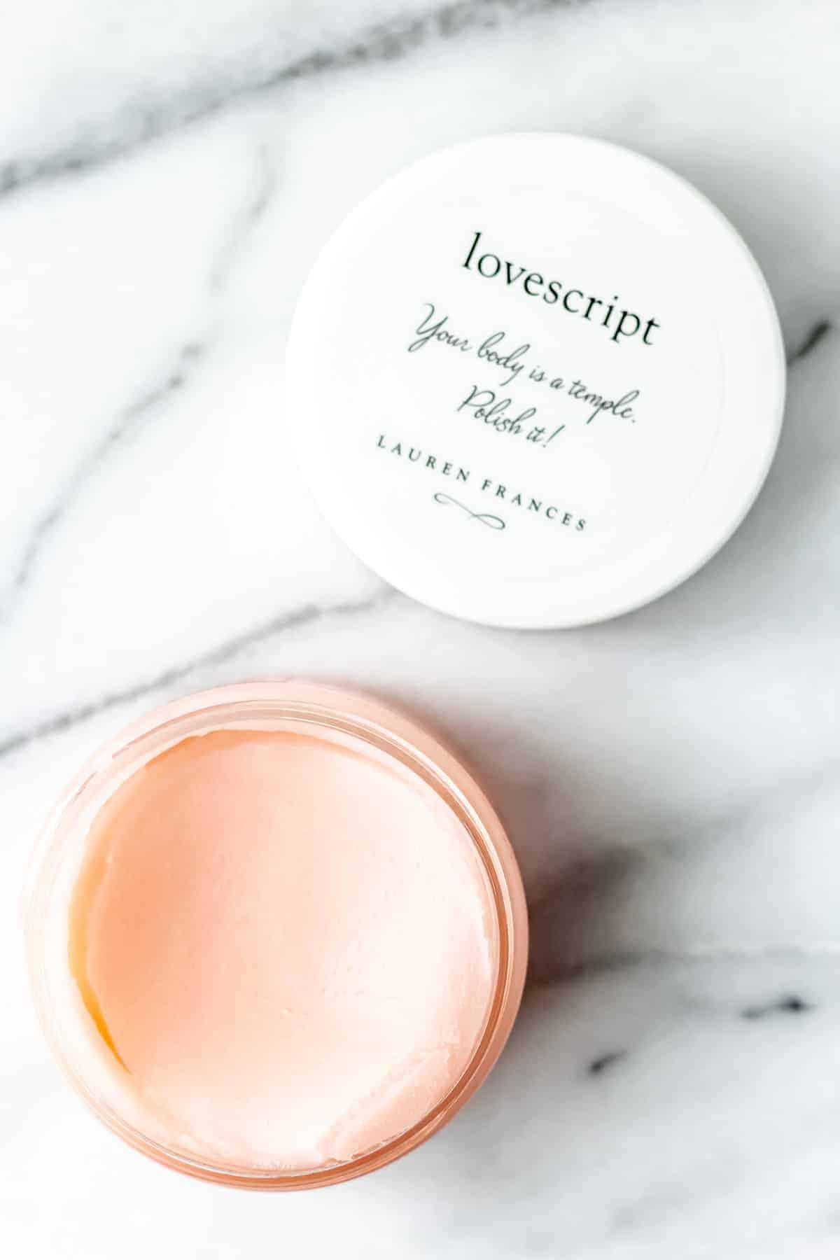 overhead of lovescript sugarplum body polish with the lid next to it on a marble background