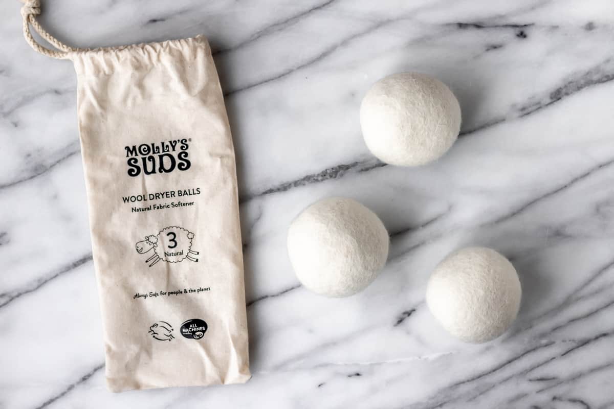 3 Molly's Suds Natural Wool Dryer Balls and their bag on a marble background.