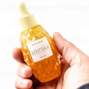 A hand holding a bottle of Glow Recipe Pineapple-C Bright Serum.