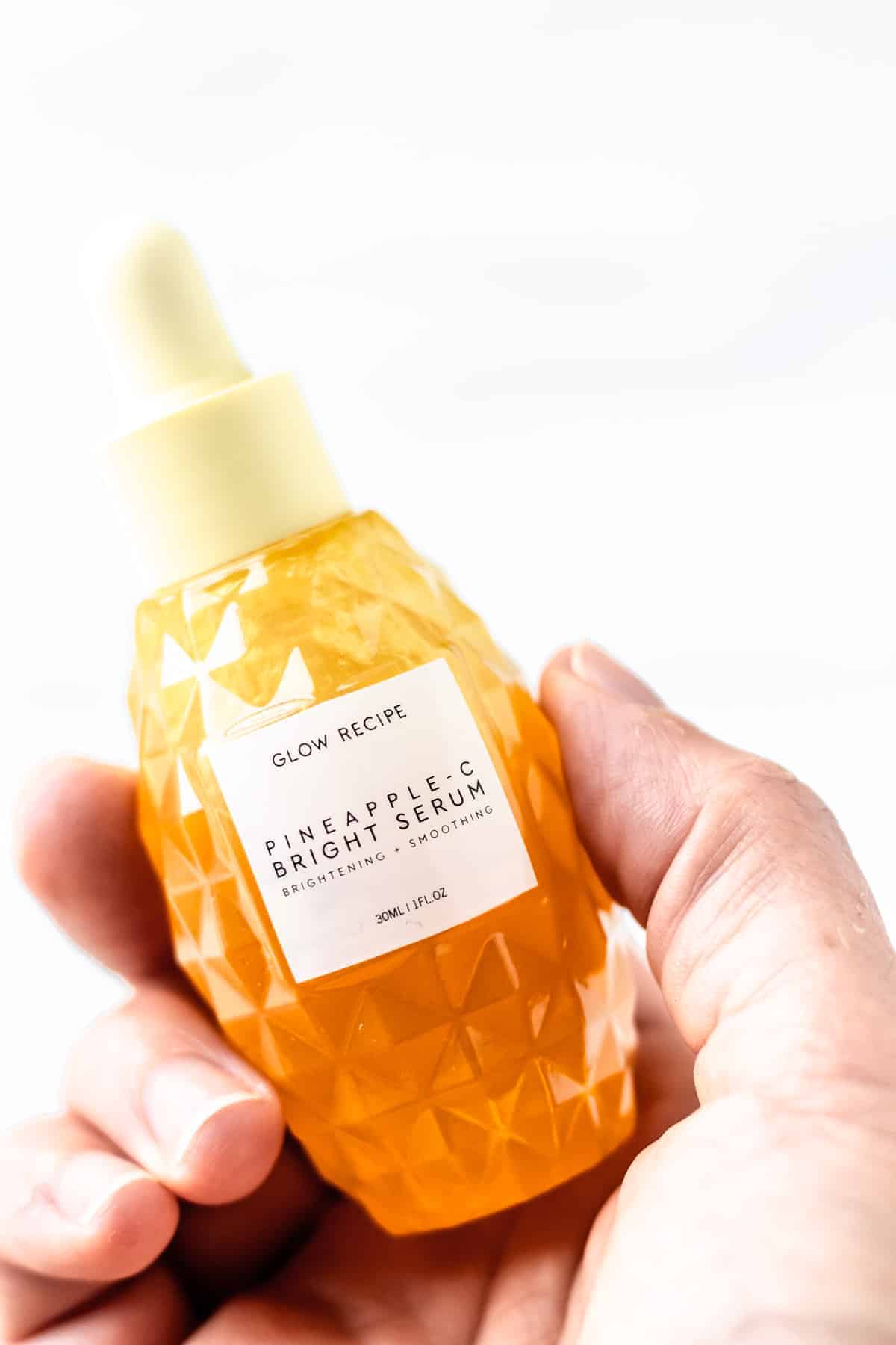 A hand holding a bottle of Glow Recipe Pineapple-C Bright Serum.