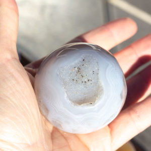 A hand holding a druzy agate sphere.