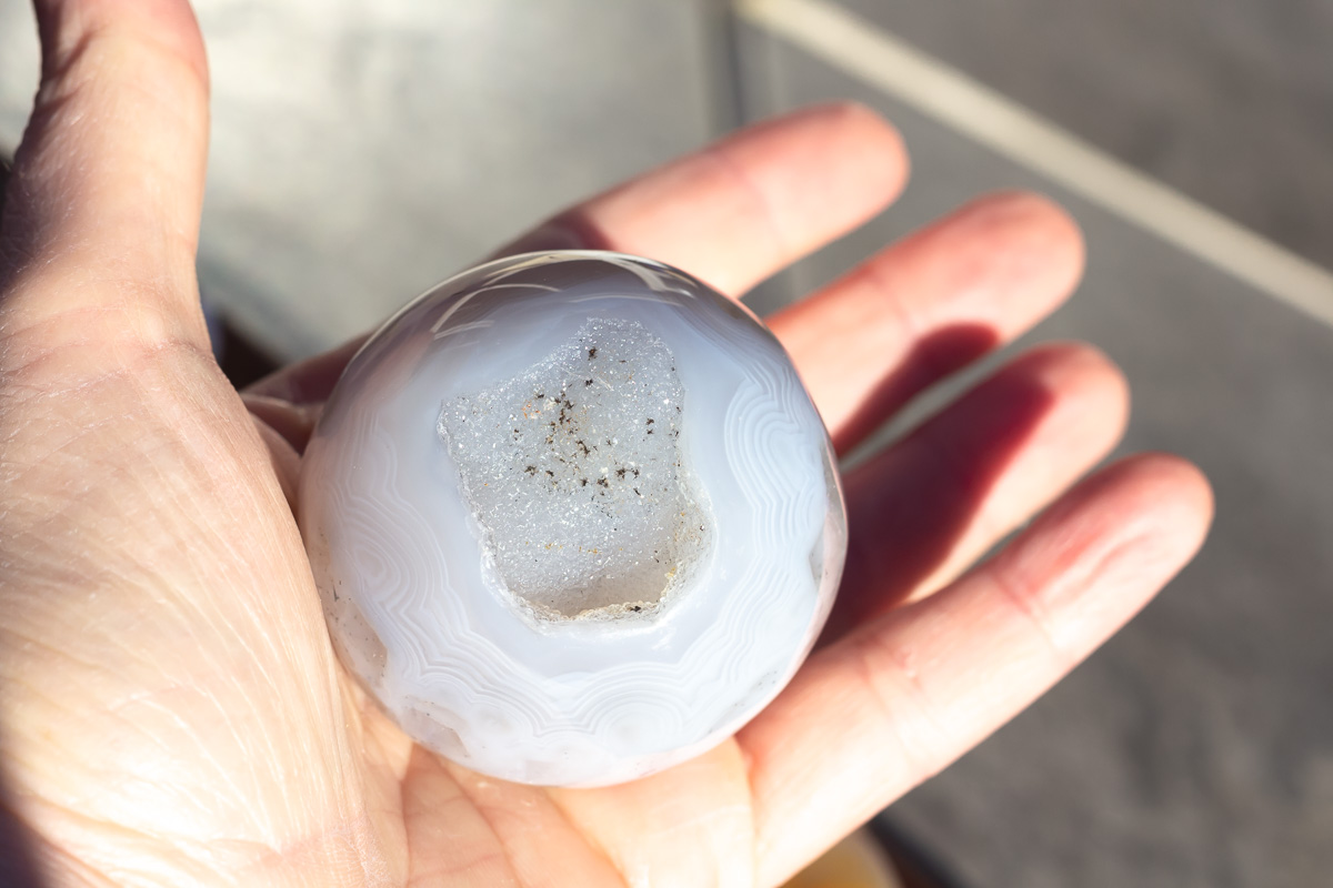 A hand holding a druzy agate sphere.