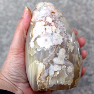 A hand holding a large flower agate crystal free form.