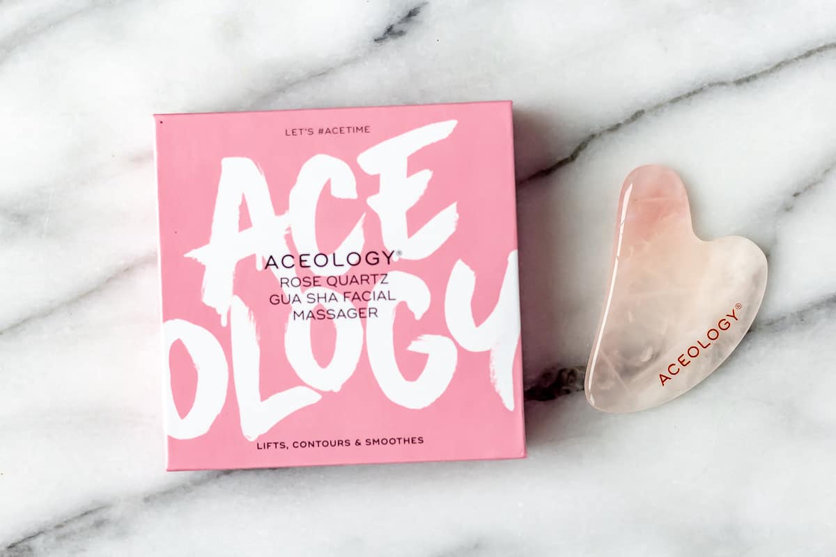 Aceology Rose Quartz Gua Sha Facial Massager and box on a marble background.