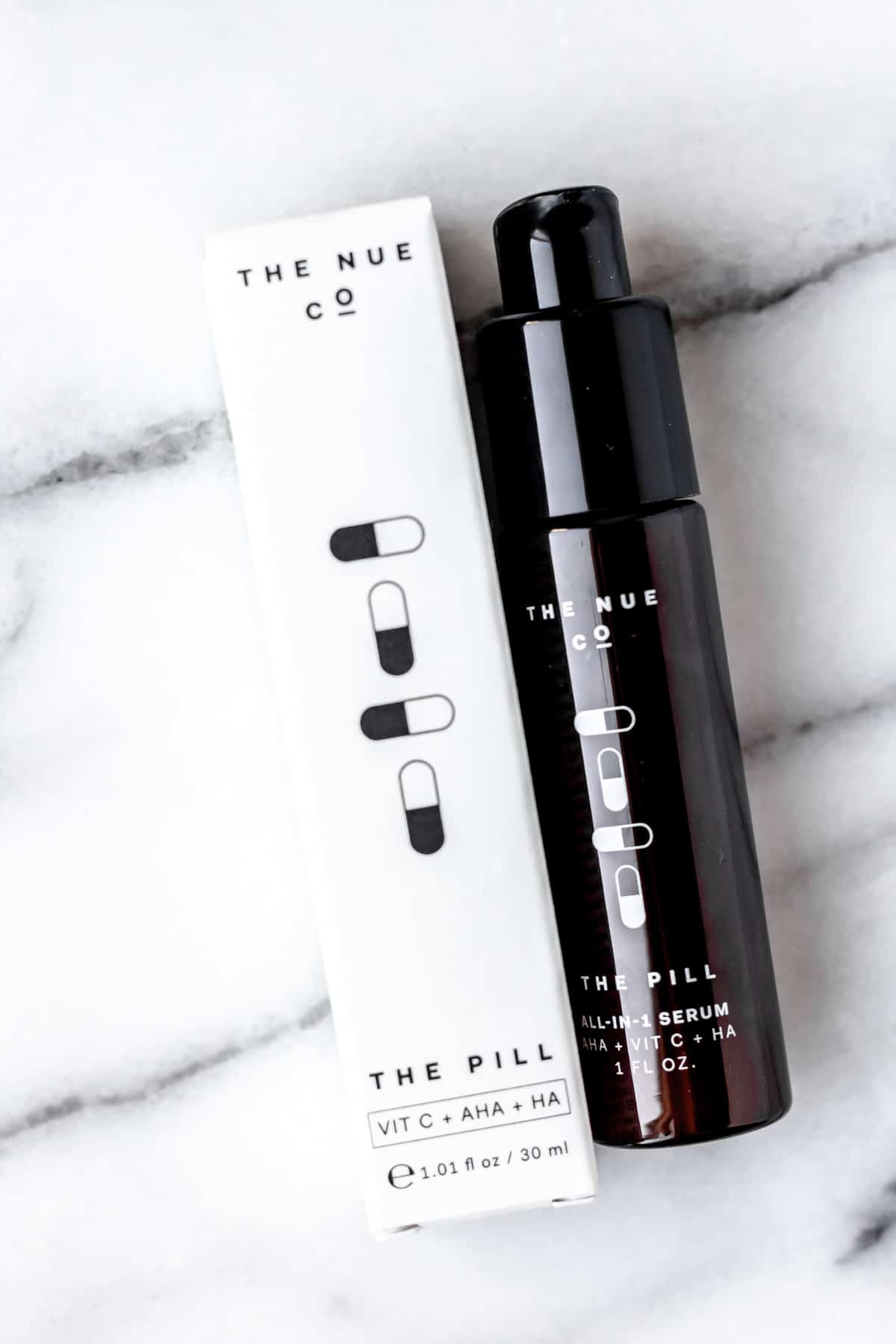 THE NUE CO The Pill All-In-One Serum bottle and box on a marble background.