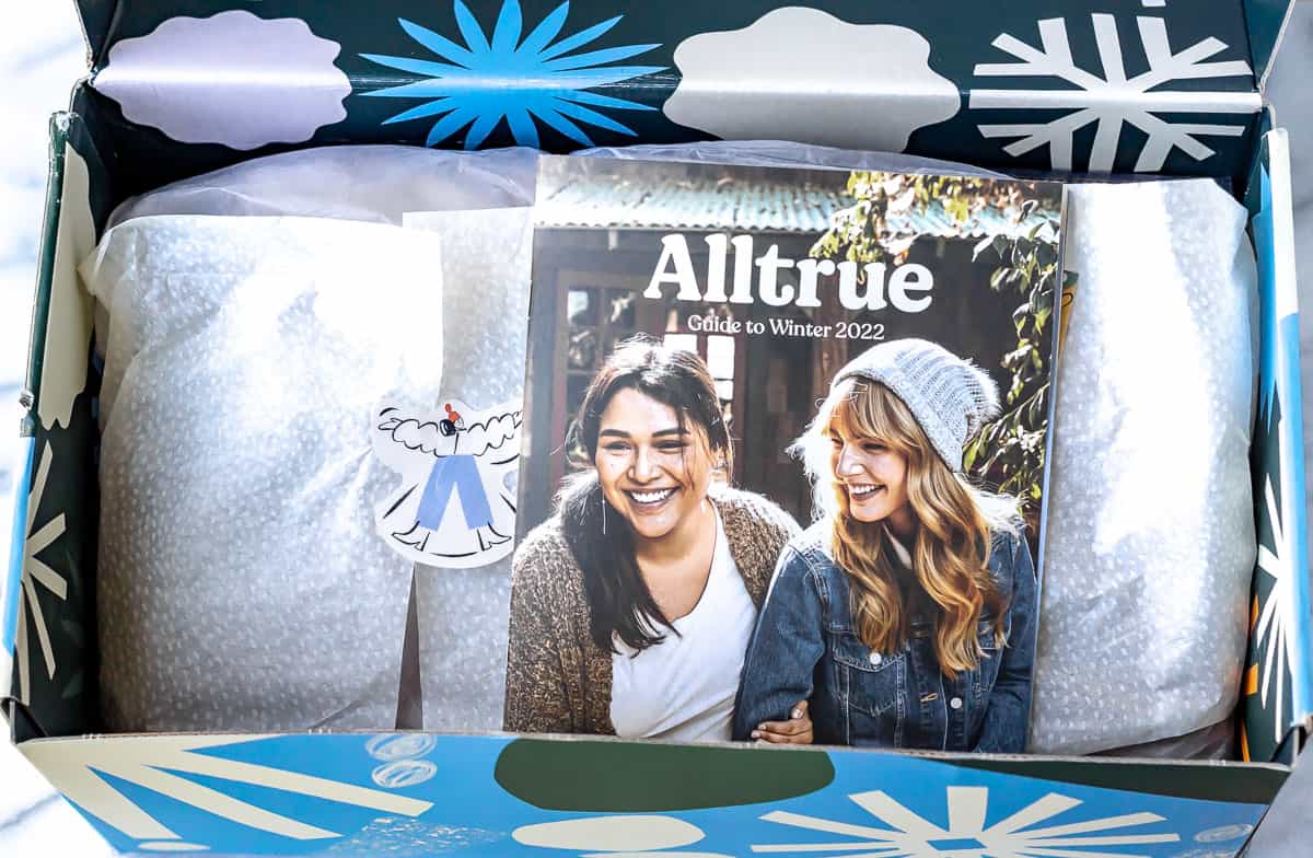 An opened winter 2022 Alltrue with the magazine on top of items wrapped in tissue paper.