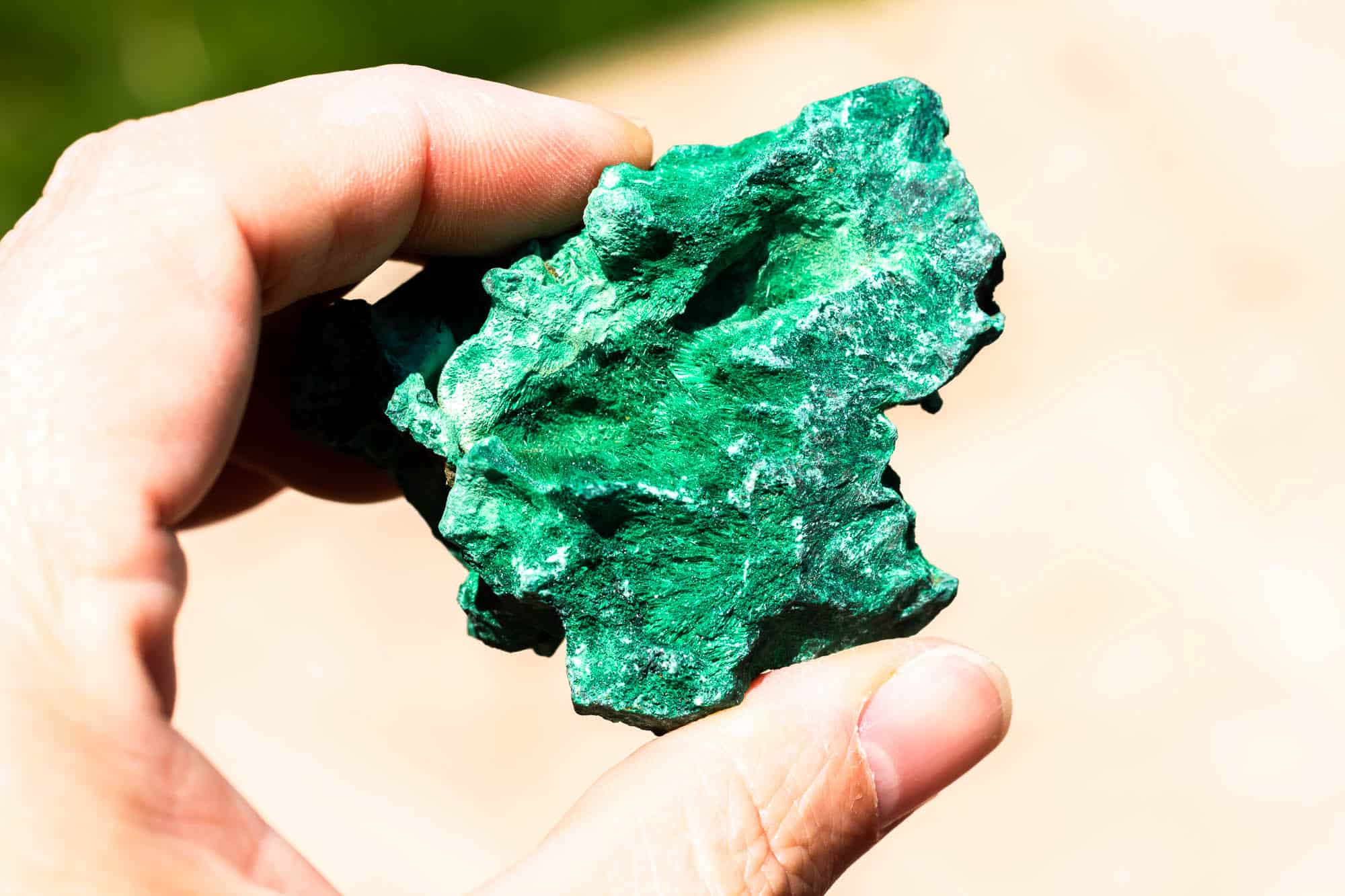 A hand holding up a piece of raw malachite.