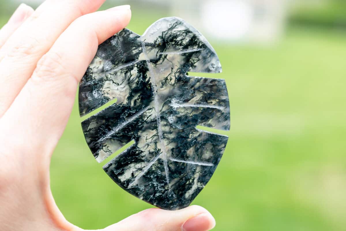Hand holding up a moss agate. leaf carving.
