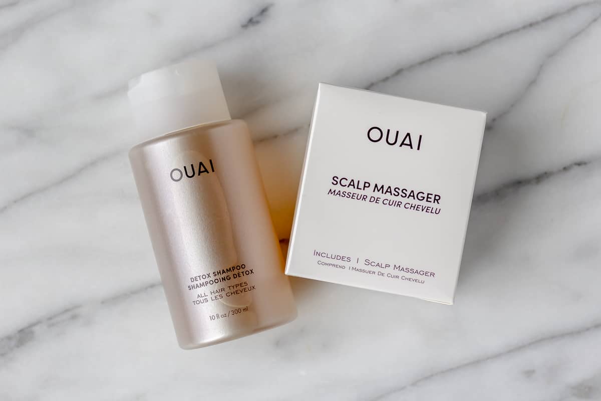 Quai Shampoo bottle and a box that says scalp massager on it on a marble background.