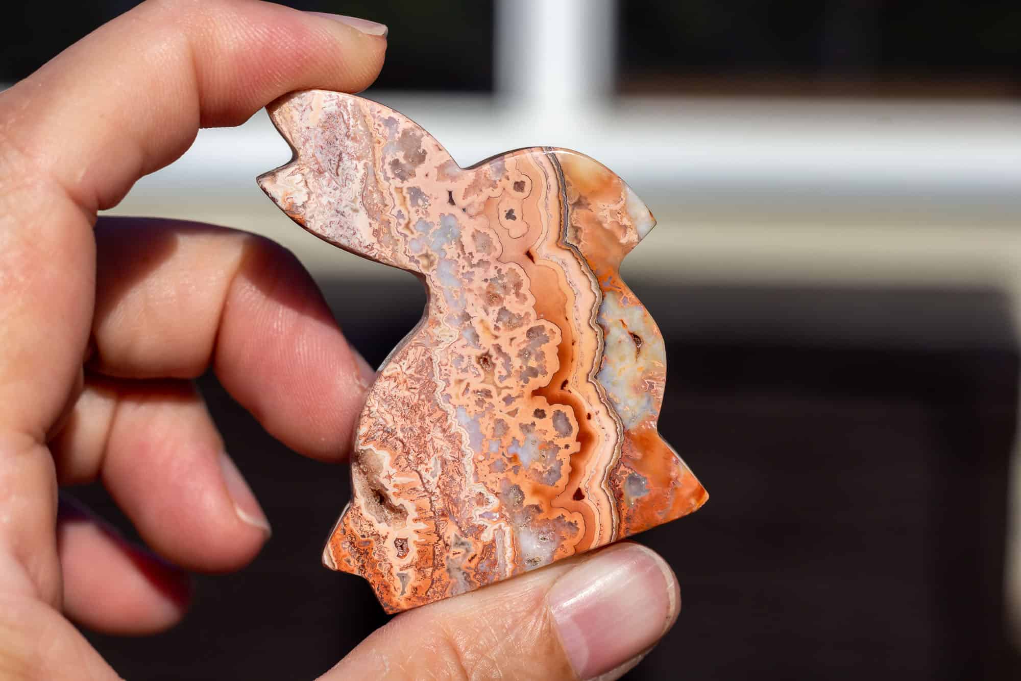 A hand holding a pink crazy lace agate rabbit carving.