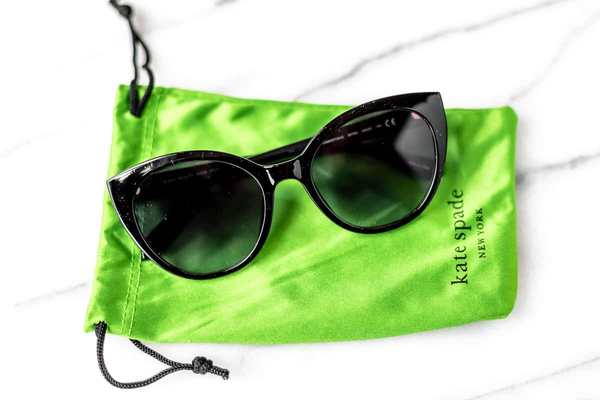 Black cat eye Kate Spade sunglasses sitting on a green cloth pouch.