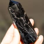 A hand holding up a black tourmaline tower with text overlay.