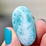 An oval larimar cabochon being held up with text overlay.