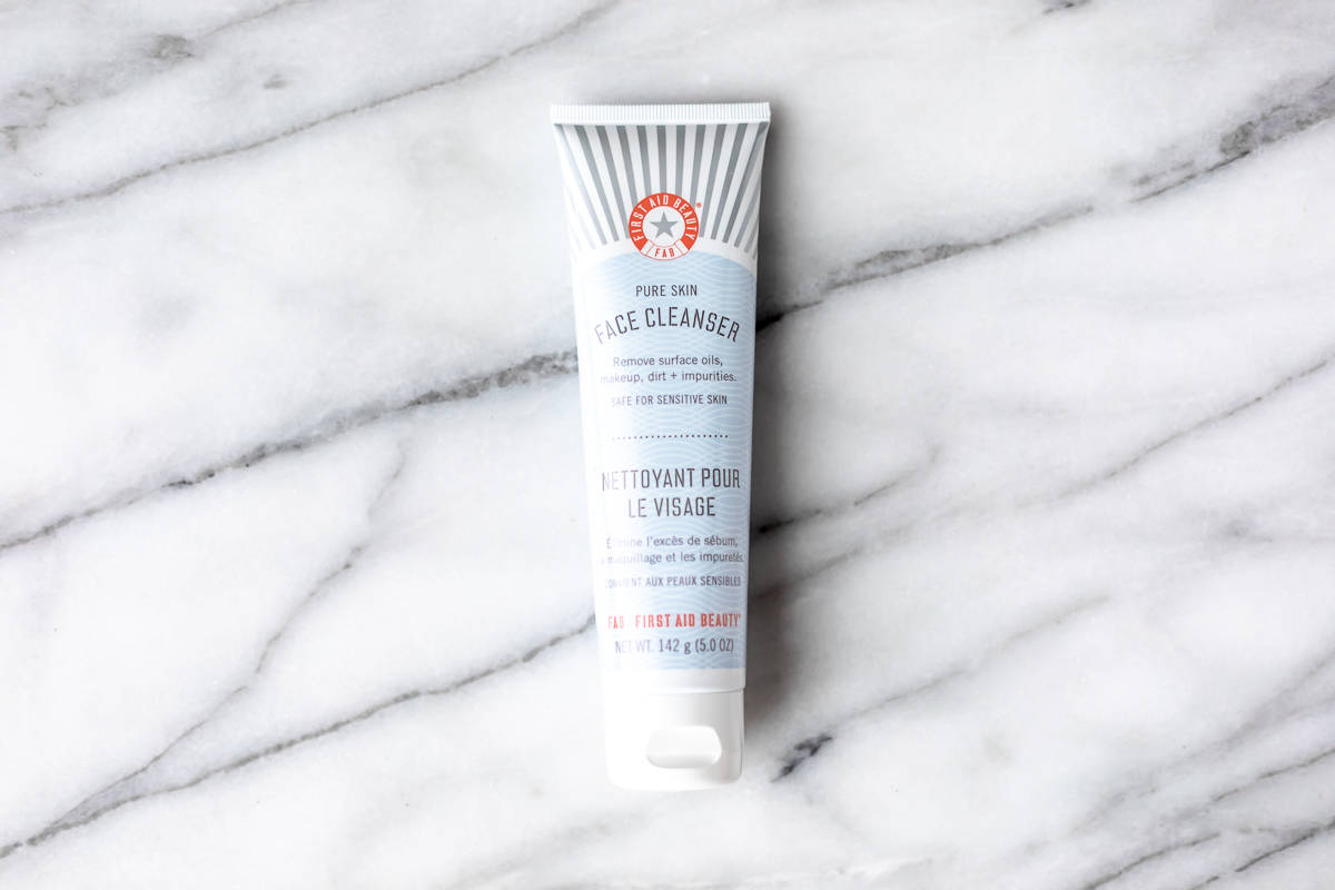 First Aid Beauty facial cleanser tube on a marble background.