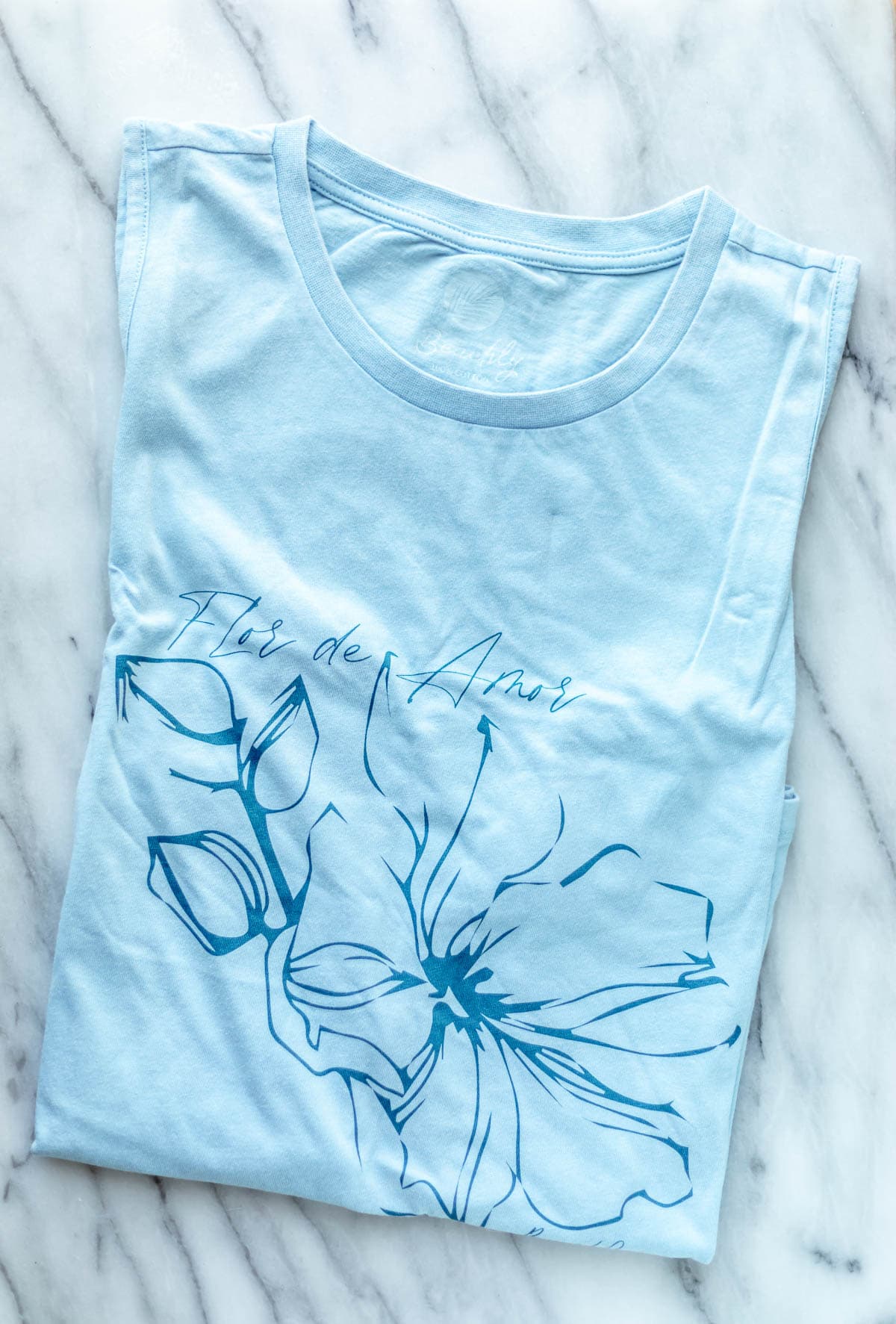 A blue tank top with a flower on it over a marble background.