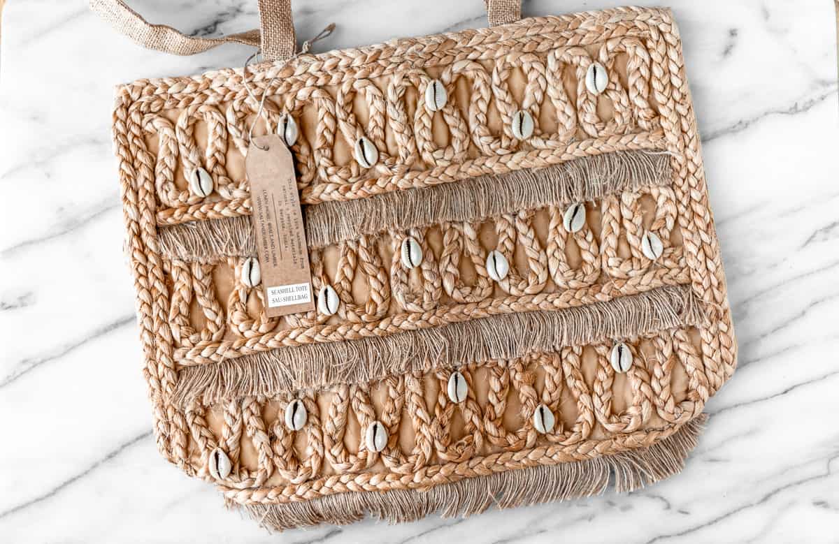 A jute tote bag with small seashells sewn into it.