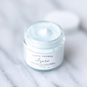 A jar of Earth Harbor Azure Regenerative Neck Cream with the lid off sitting behind it.