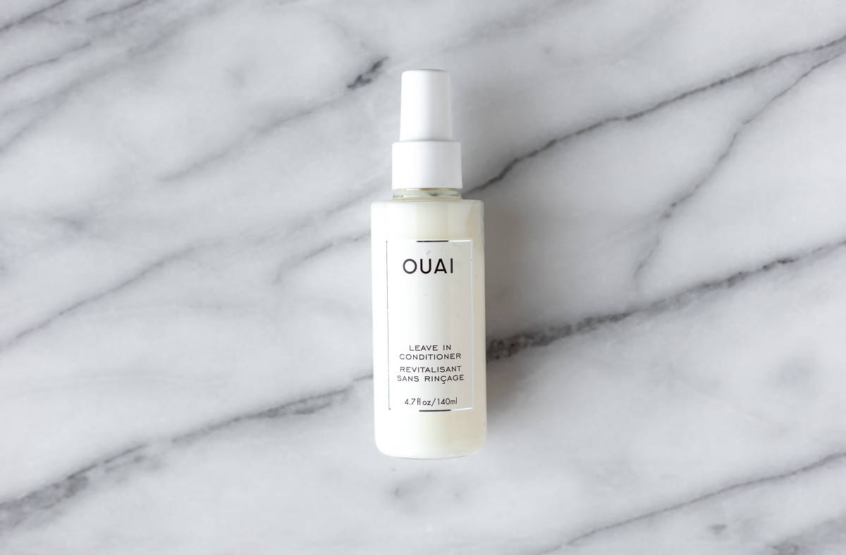 Ouai leave-in conditioner bottle on a marble background.