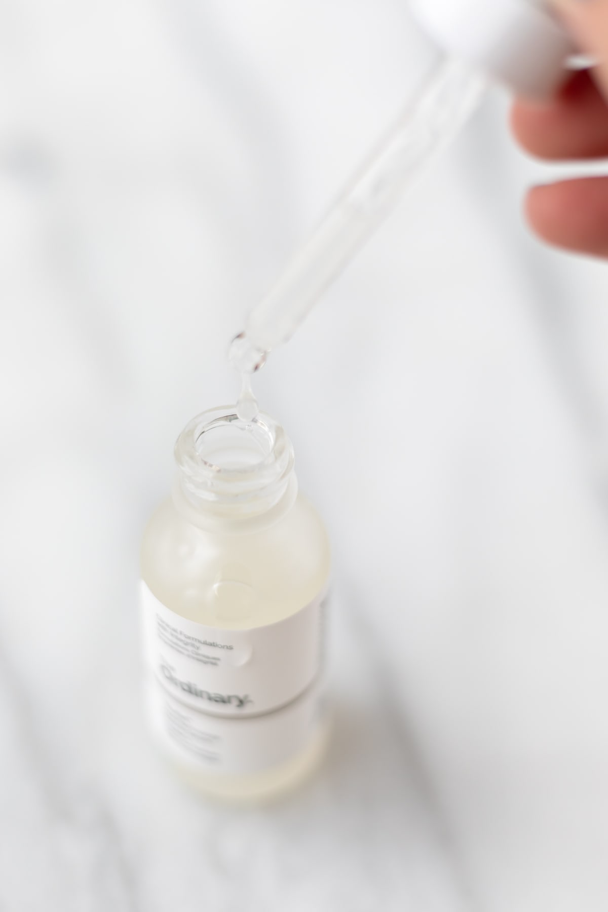 A dropper with a drop of liquid being held over a The Ordinary Multi-Peptide serum bottle.
