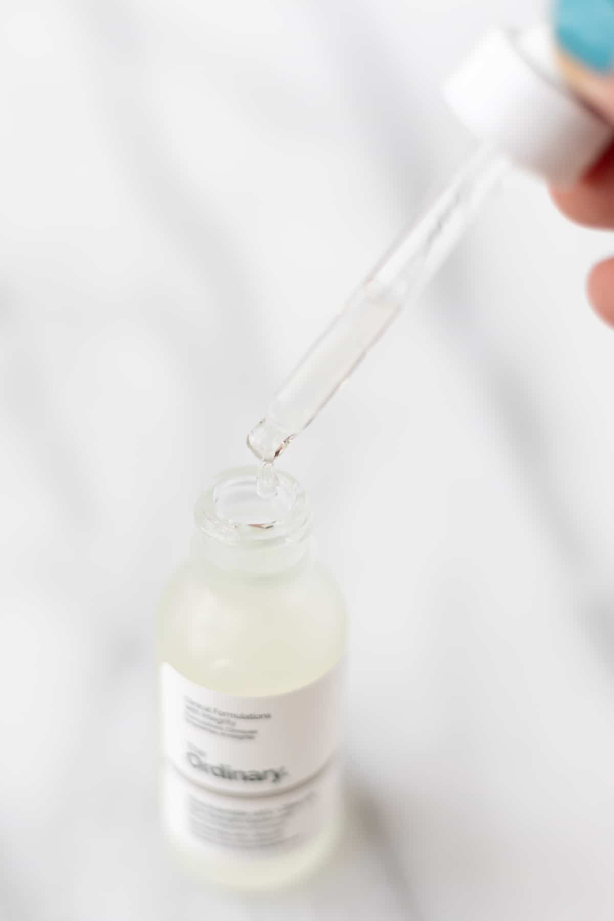 A dropper with a drop of niacinamide coming off of it over a bottle of The Ordinary Niacinamide.