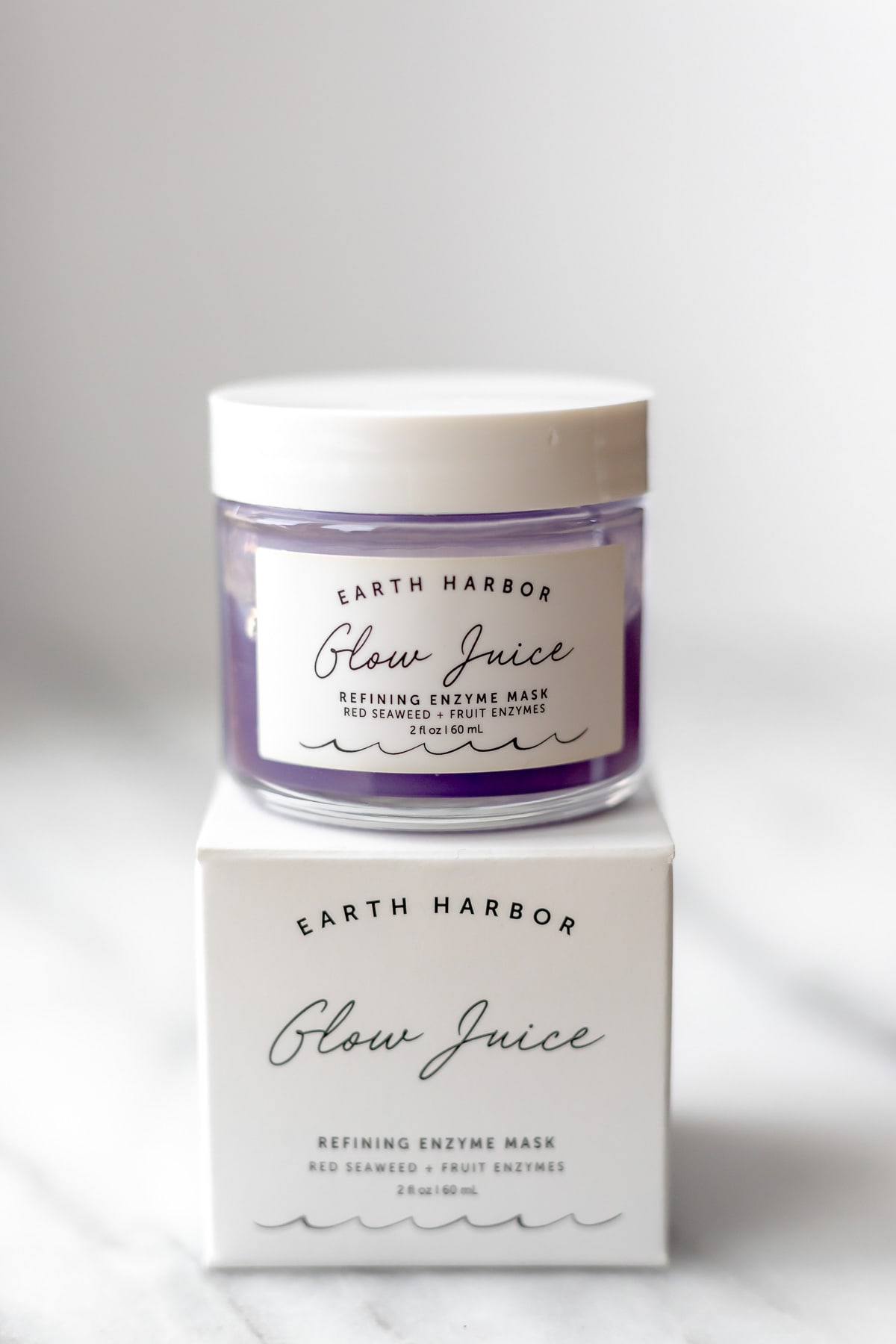 A jar of Earth Harbor Glow Juice on top of the box it comes on on a light background.