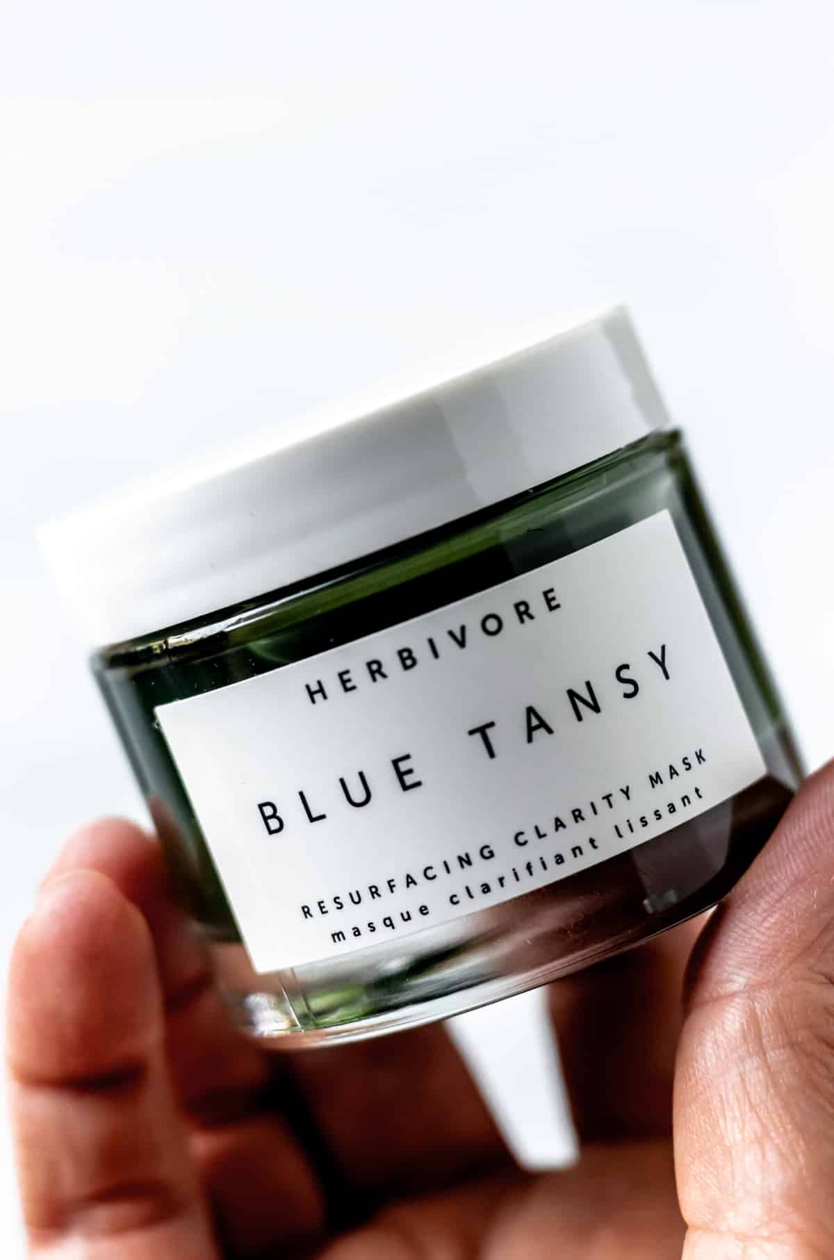 A hand holding up a jar of Herbivore Blue Tansy face mask.