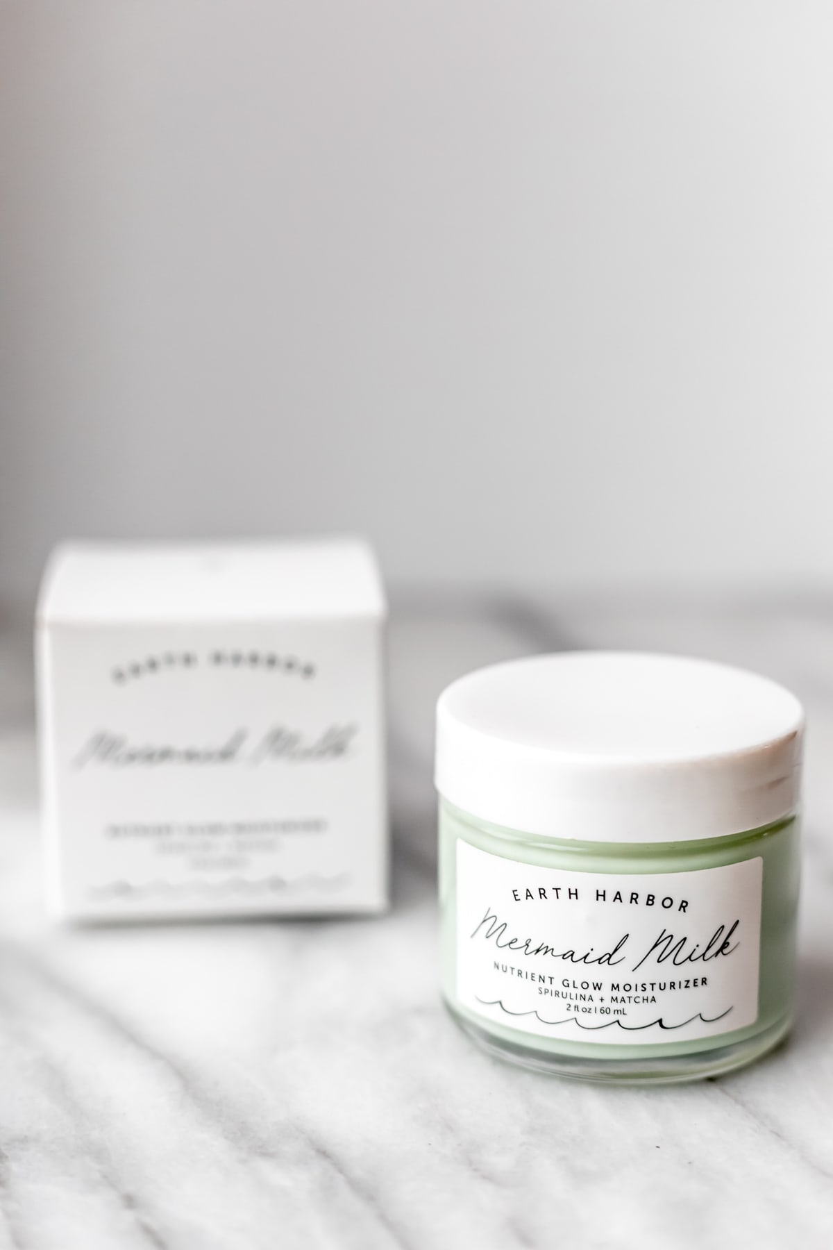 A jar and the box it comes in for Earth Harbor Mermaid Milk nutrient glow. moisturizer on a marble background.