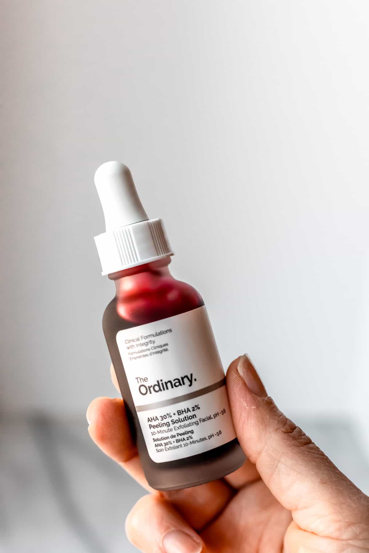 A hand holding up a bottle of The Ordinary Peeling Solution in front of a light background.