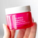 A hand holding up a jar of ELEMIS Midnight Facial over a light background with text overlay.