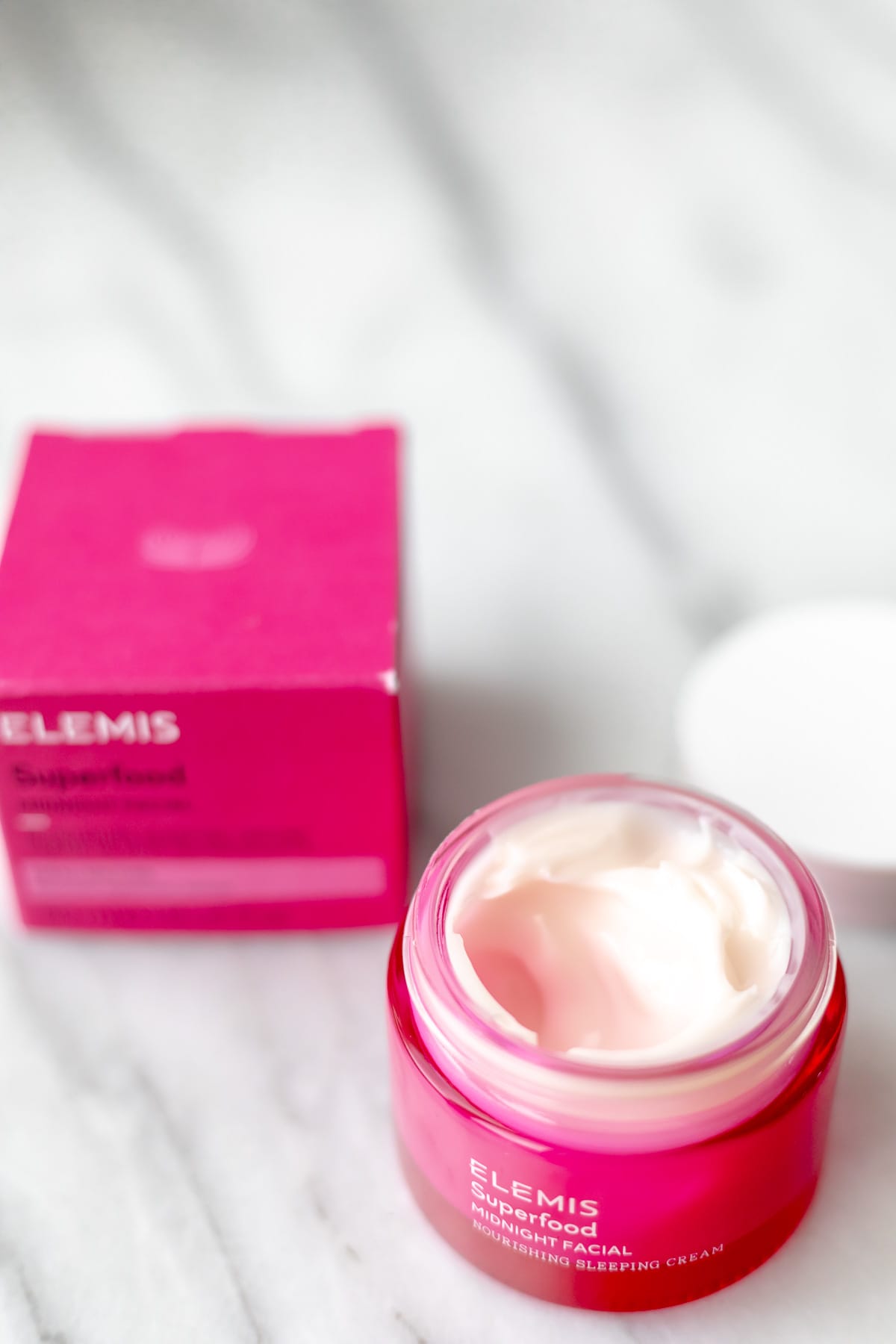 An opened jar of ELEMIS Midnight Facial with the box behind it on a marble background.