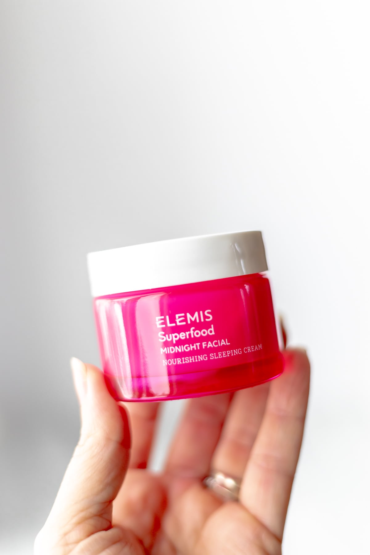 A hand holding up a jar of ELEMIS Midnight Facial over a light background.
